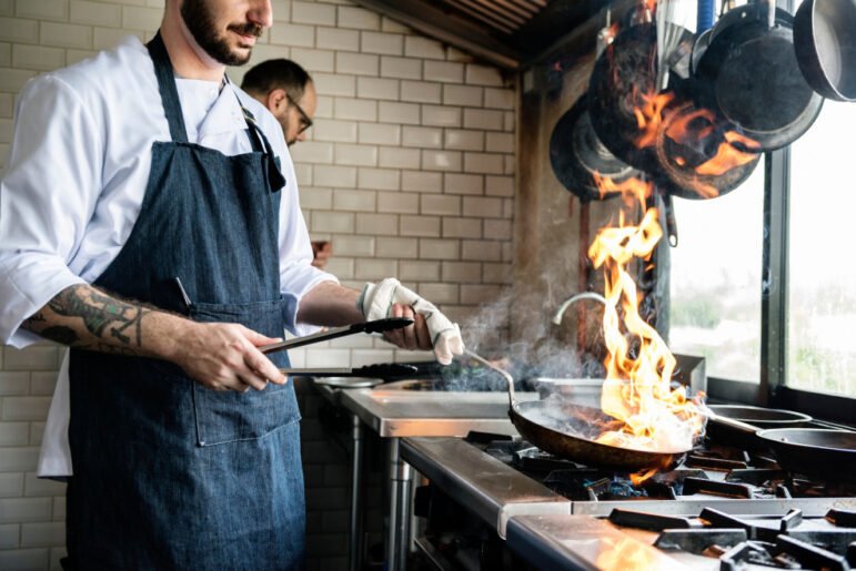 Chef cooking with a flaming a pan on a stove