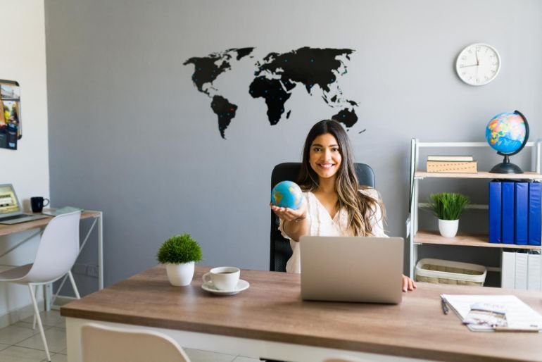 Smiling woman sat at an office desk holding a globe