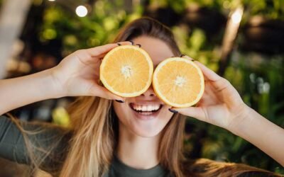 Smiling woman holding two orange halves in front of her eyes