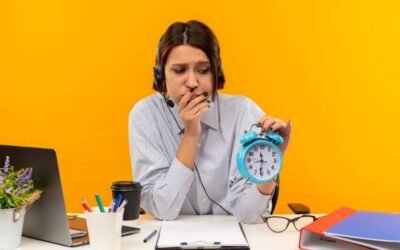 A woman sat at a cluttered desk holding a blue alarm clock