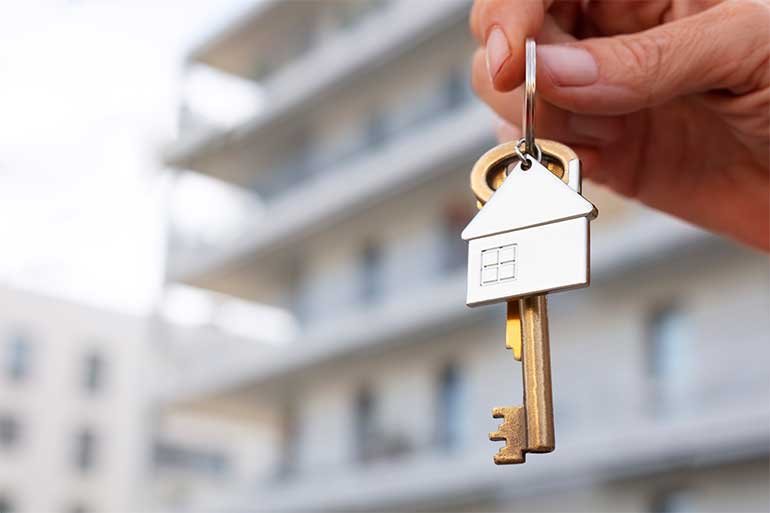 Person holding up a key and chain with a small metal house keyring