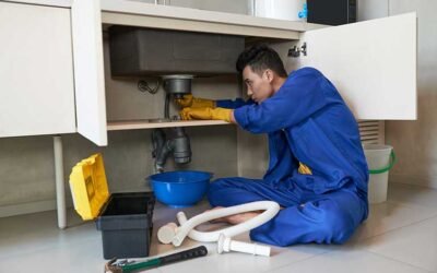 Plumber under a sink clearing a blocked drain pipe