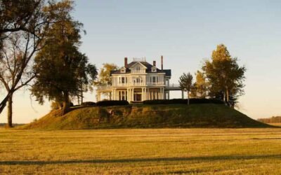 A traditional white home standing on a mound in the middle of a field