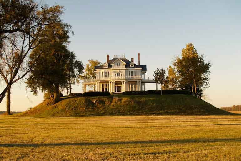 A traditional white home standing on a mound in the middle of a field