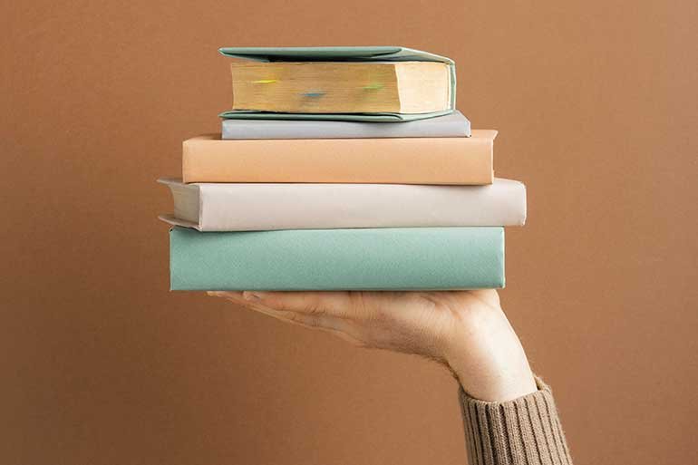 A person holding up a pile of books in one hand