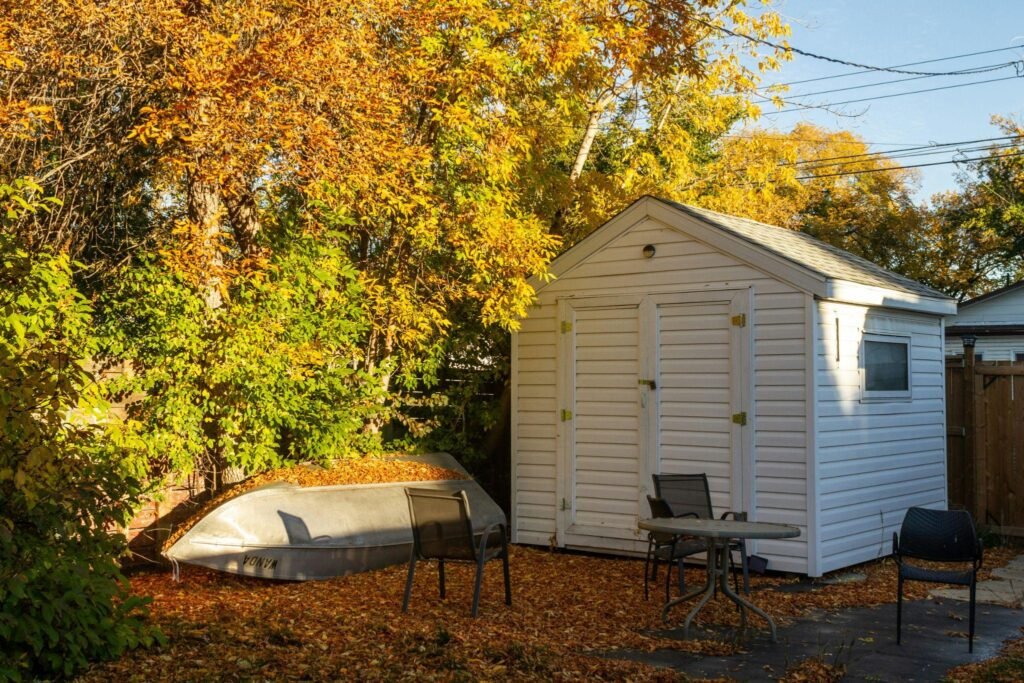 A garden showing a large white storage shed amongst fallen autumnal leaves